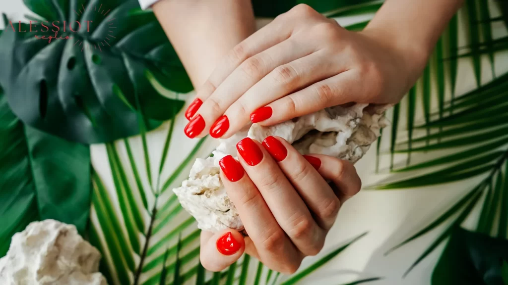 Bright red gel nails held against a decorative background, answering the question of how long do gel nails last with bold, lasting color.